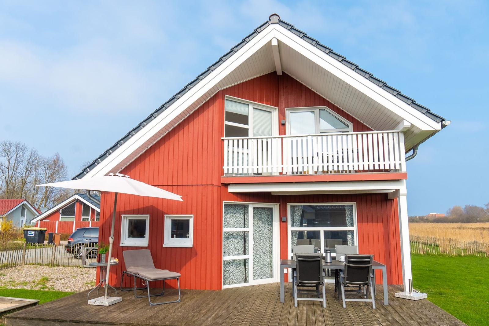Rotes Ferienhaus mit Balkon und Terrasse mit Sitzgelegenheiten.