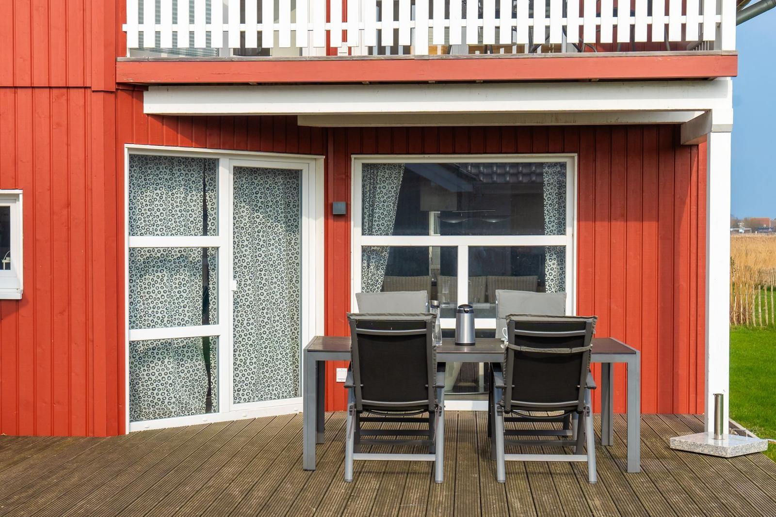 Roter Holzaufbau mit Terrasse, Tisch und Stühlen sowie Fenstern mit Vorhängen.
