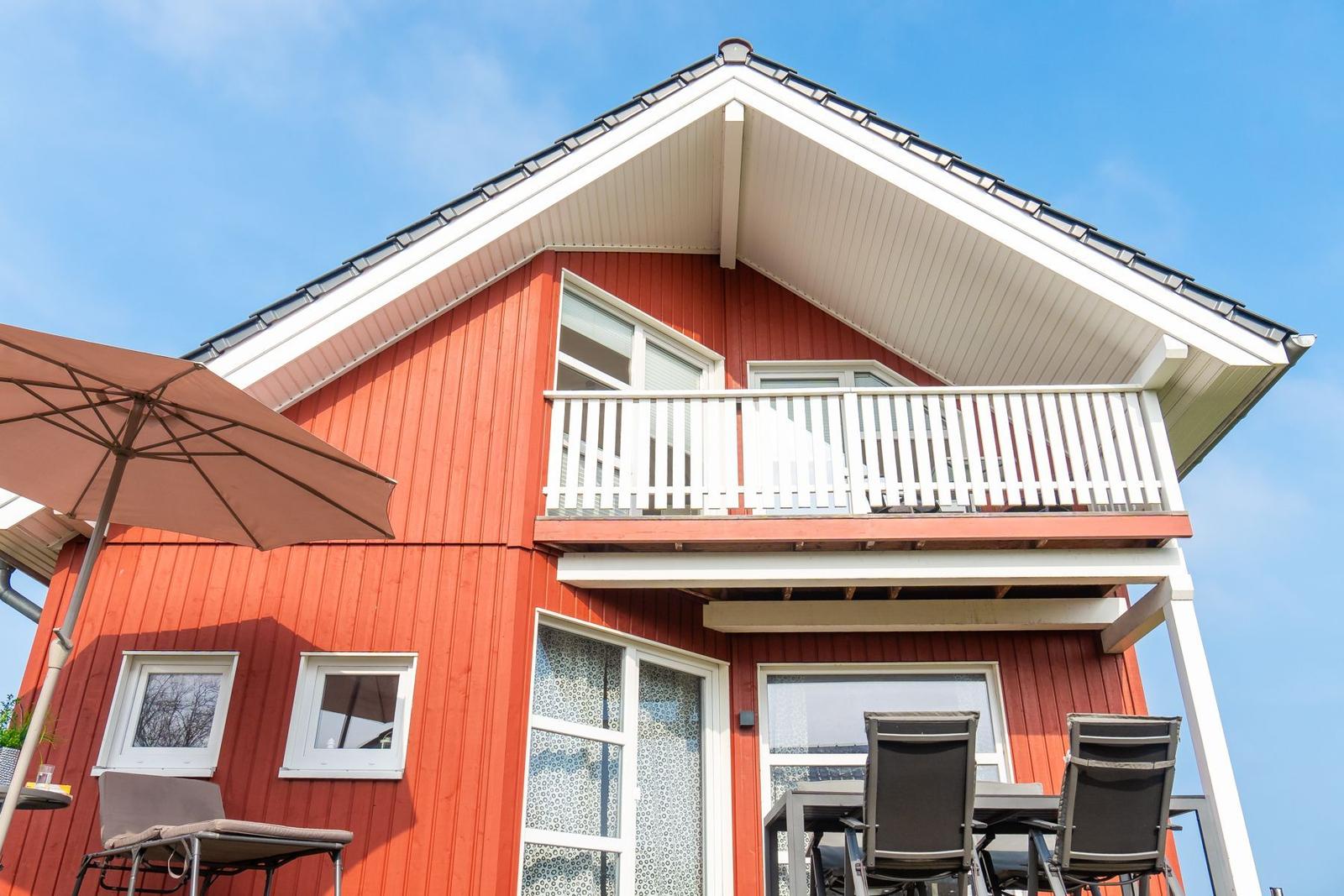 Rotes Haus mit Balkon und Terrasse unter blauem Himmel.