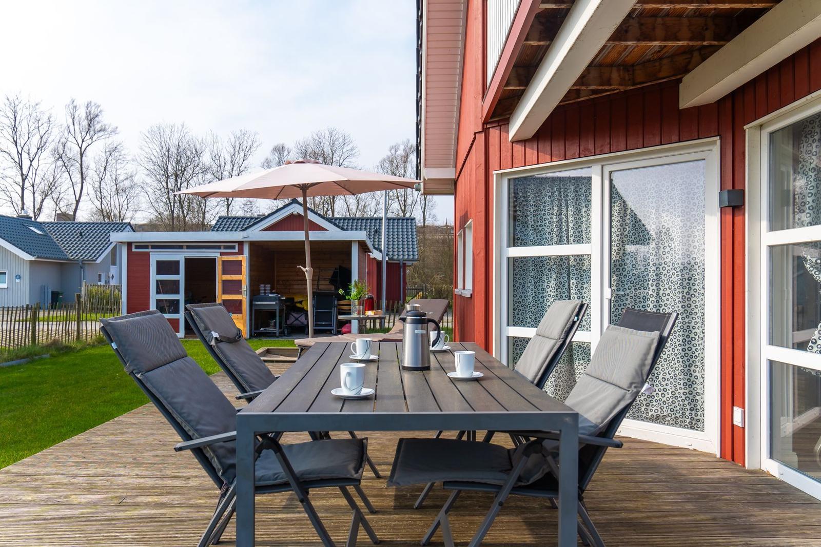 Terrasse mit Tisch, Stühlen und Sonnenschirm neben rotem Haus