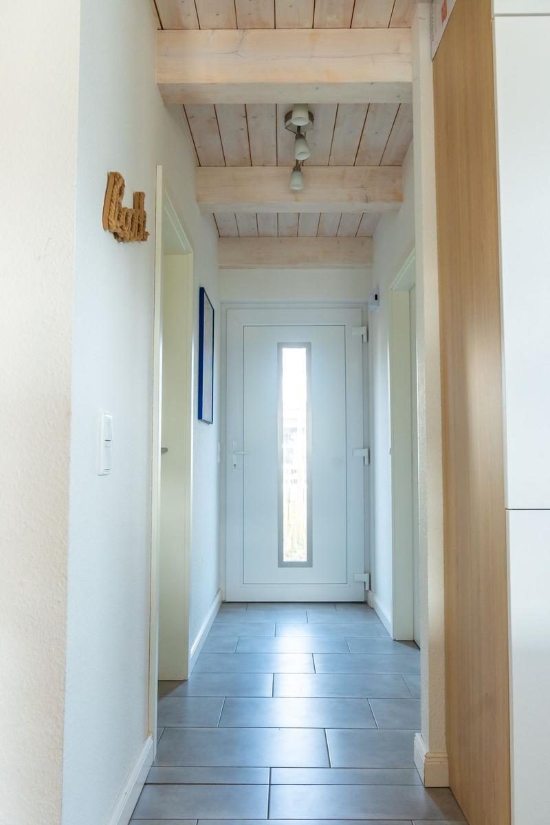 Flur mit Holzdecke, Fliesenboden und weißer Tür mit Glasstreifen.