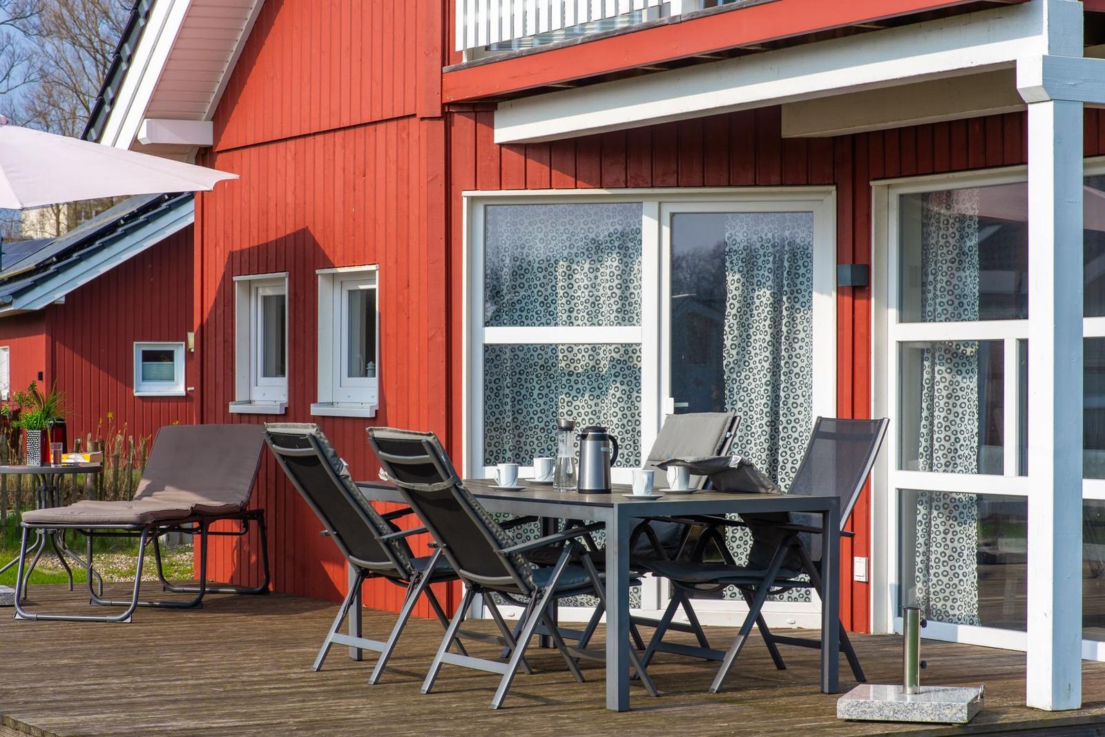 Roter Holzhaus mit Terrasse, Tisch, Stühle und Sonnenschirm
