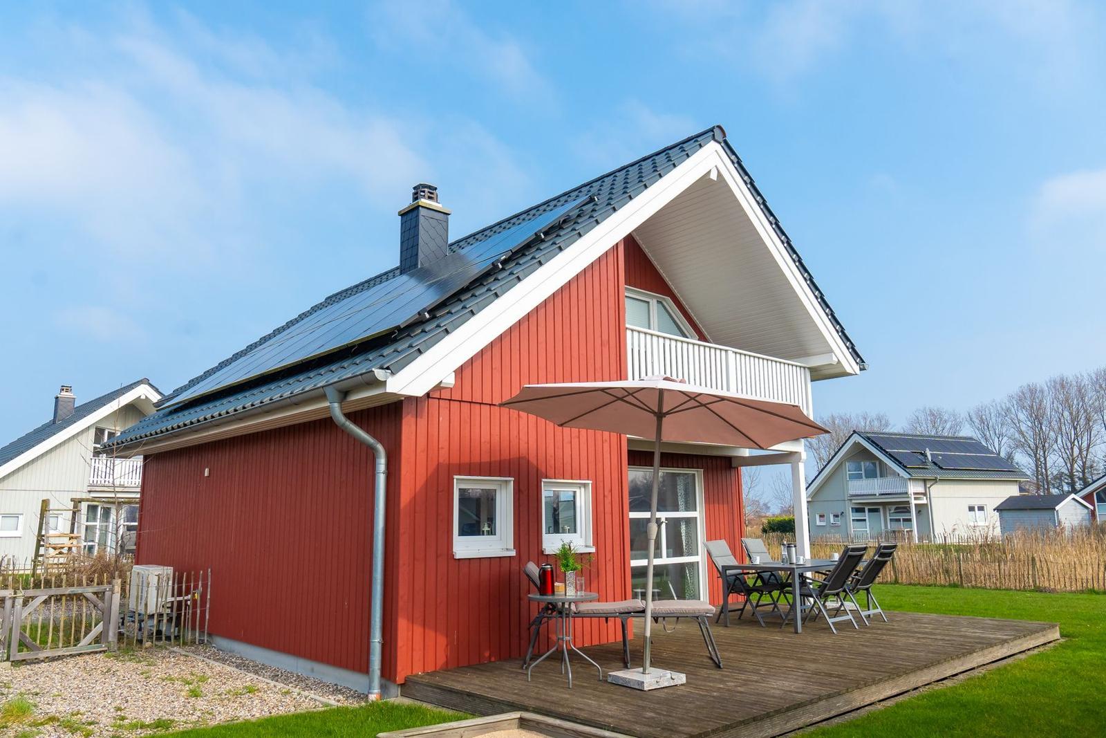 Rotes Ferienhaus mit Balkon und Terrasse mit Tisch, Stühlen und Sonnenschirm.