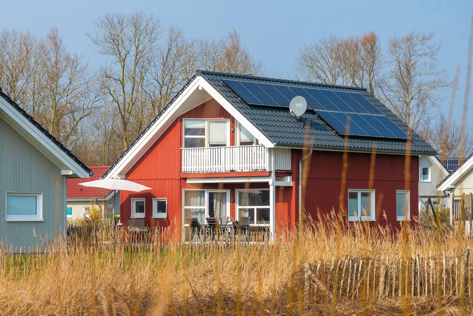 Rotes Haus mit Balkon und Solaranlage. Außenterrasse mit Tisch und Stühlen.