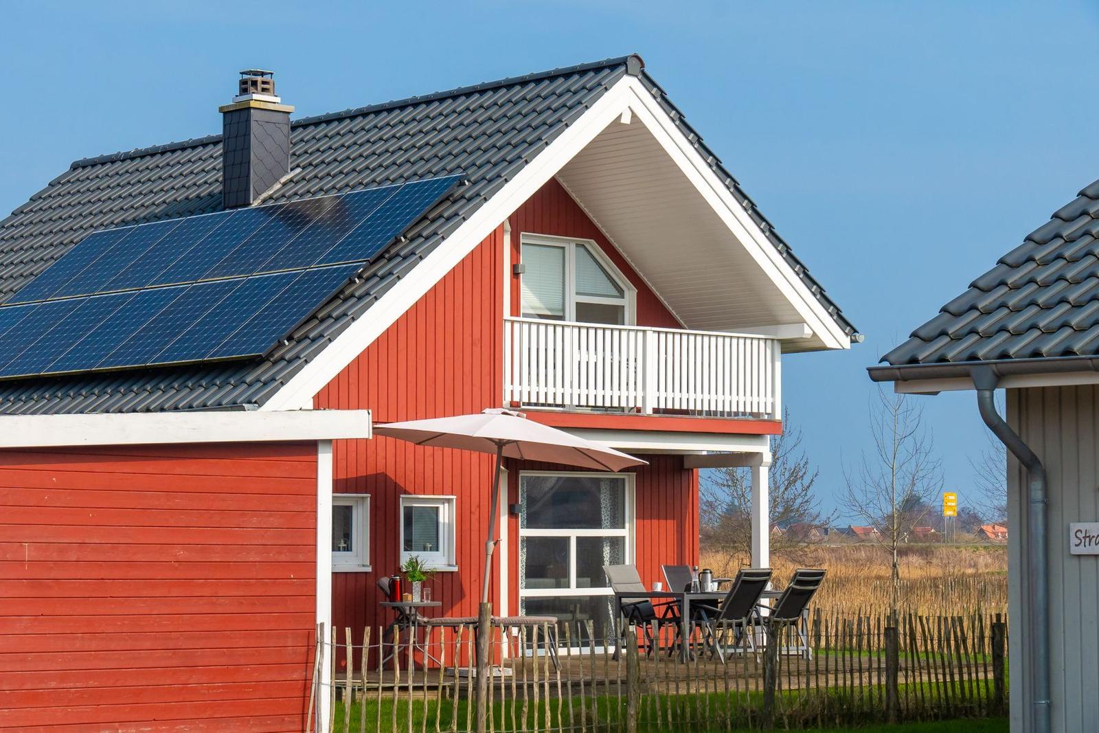 Rotes Haus mit Solaranlage und Balkon. Außenterrasse mit Tisch und Stühlen.