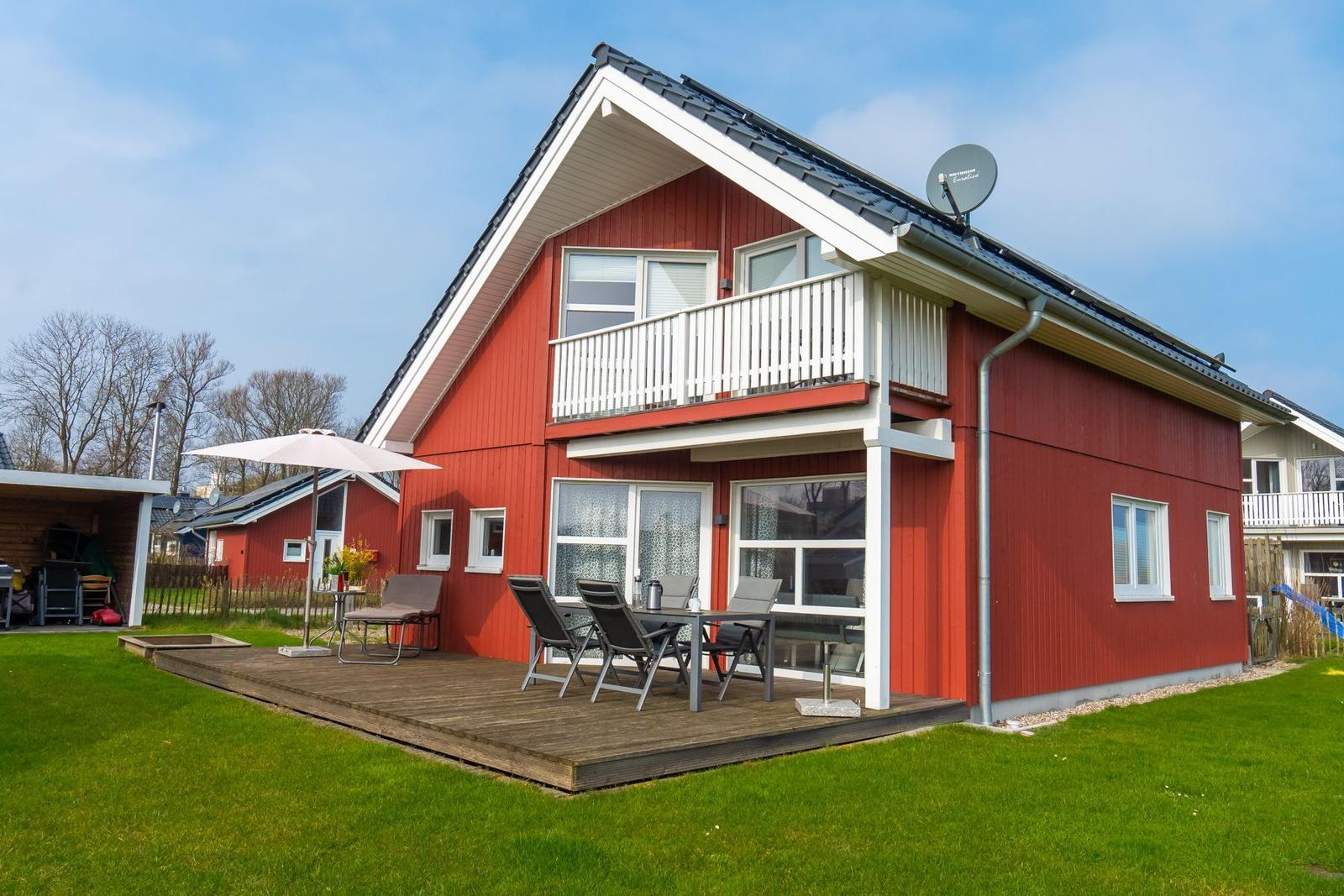 Rotes Ferienhaus mit Balkon und Terrasse mit Gartenmöbeln.