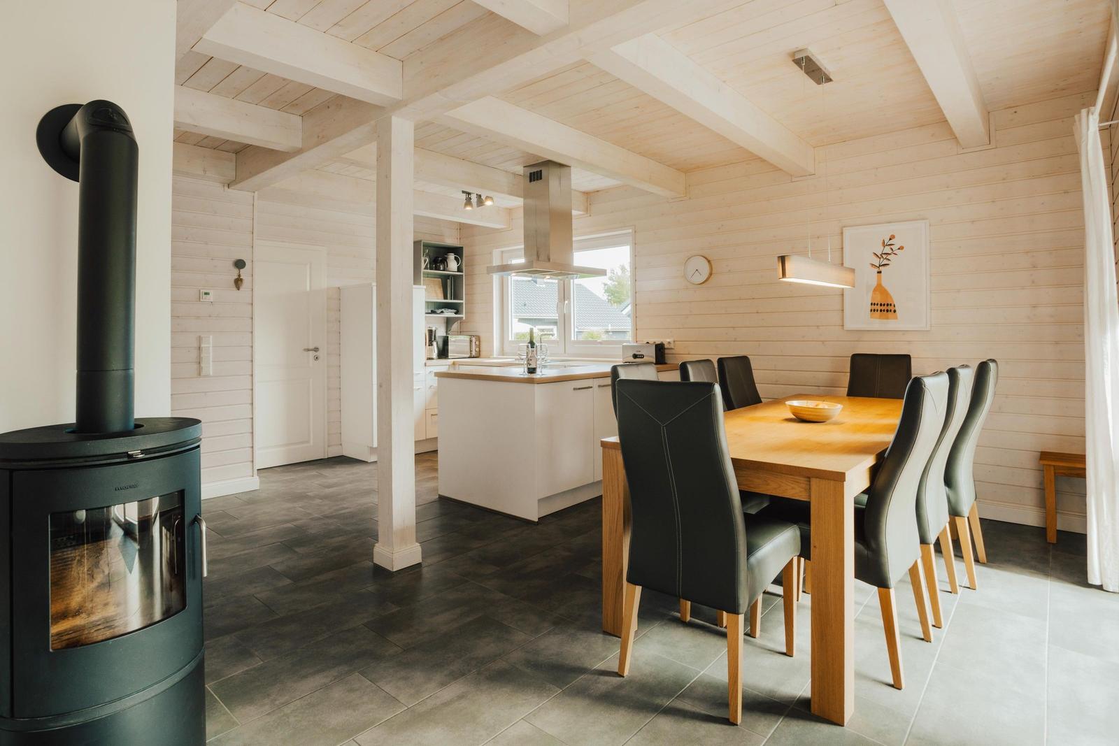 Essbereich mit Holztisch und Stühlen. Küche mit Insel. Holzwände und Deckenbalken.