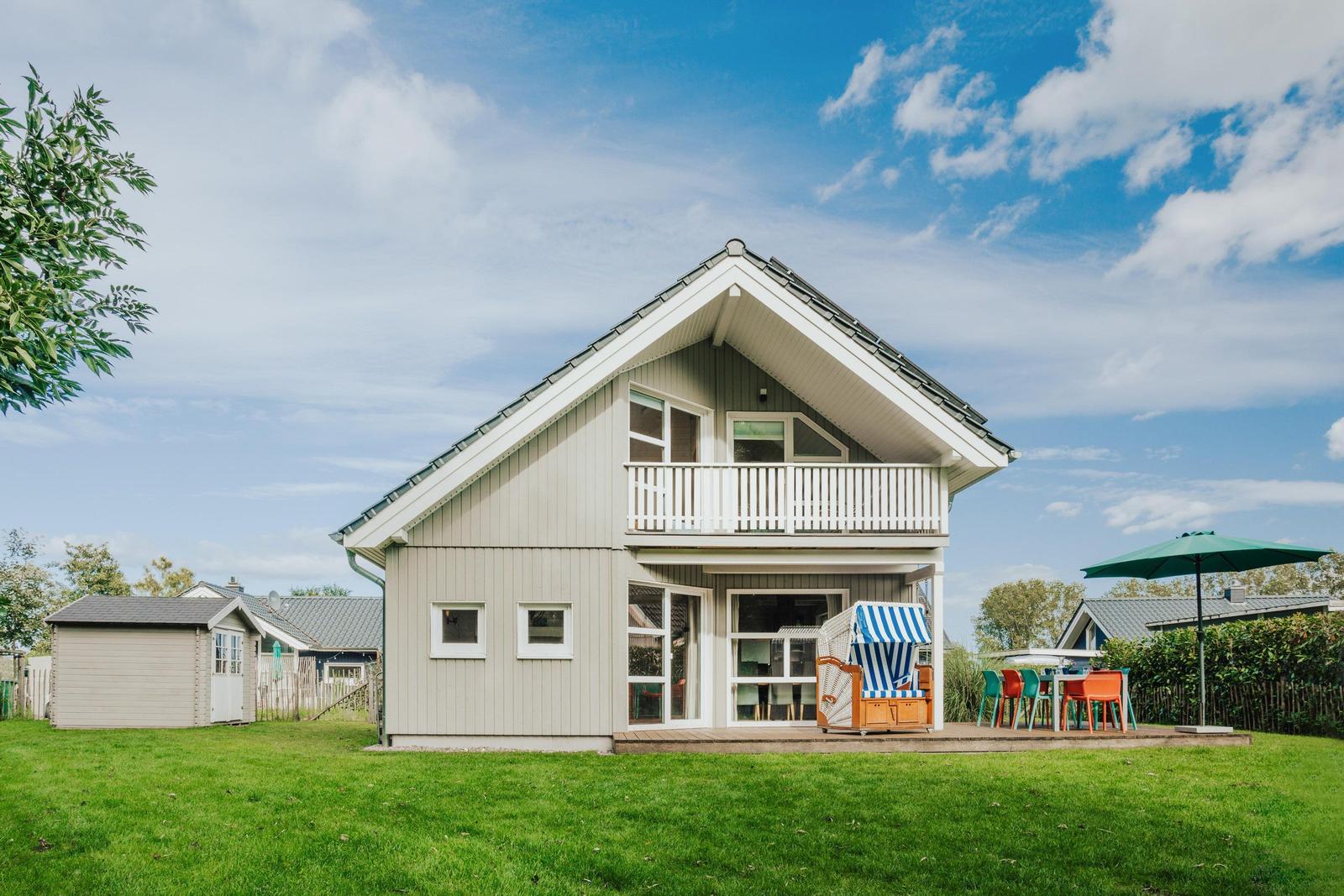Haus mit Balkon, Garten und Terrasse mit Strandkorb und Tisch.