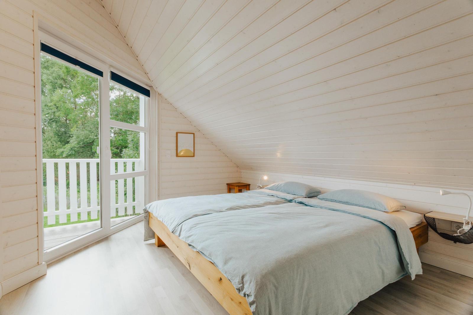 Schlafzimmer mit Doppelbett, Fenster und Balkon. Holzwände und Boden.
