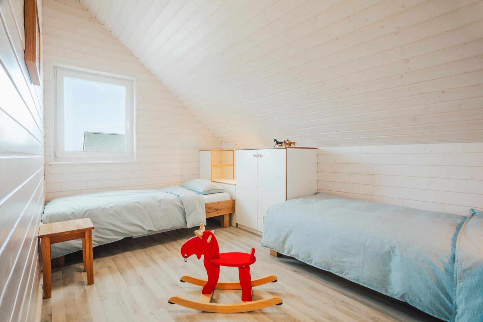Zimmer mit zwei Betten, rotem Schaukelpferd und Fenster. Holzwände und Boden.