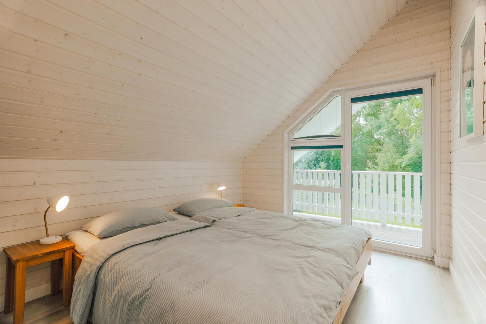 Schlafzimmer mit Dachboden, Bett, Nachttisch und Balkon mit Blick auf Bäume.