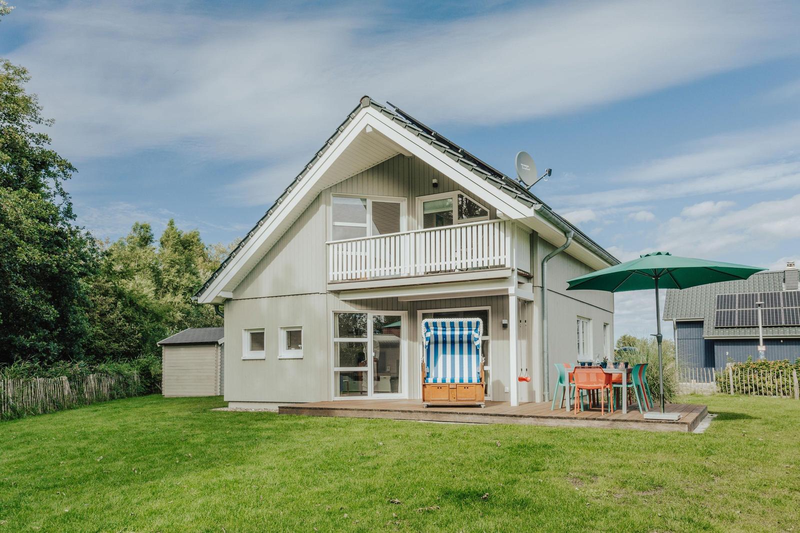 Haus mit Balkon, Terrasse und Garten. Blauer Himmel, Sonnenschirm und Strandkorb.