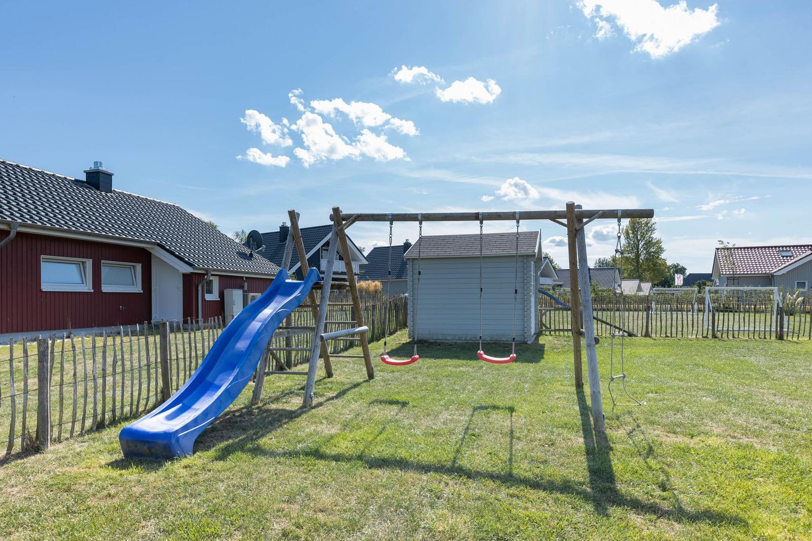 Hinterhof mit Spielplatz, Schaukel und Rutsche auf grünem Rasen.