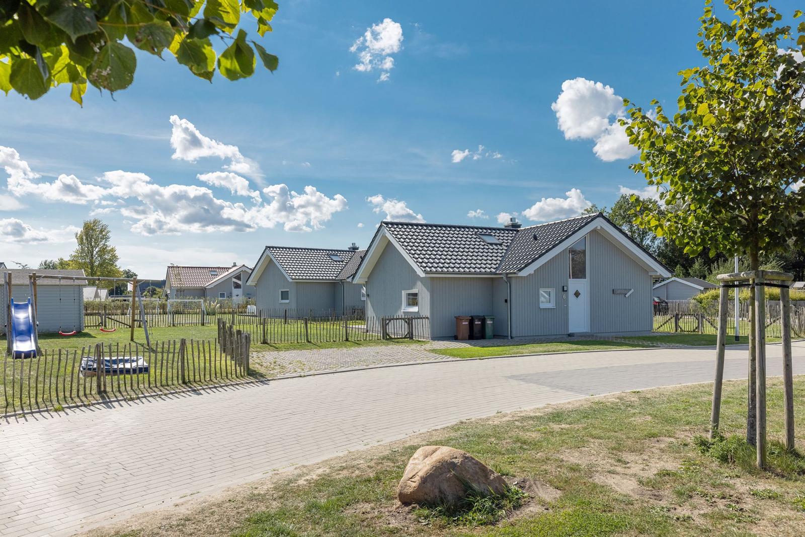 Ein modernes Ferienhaus mit Spielplatz und Garten unter blauem Himmel.