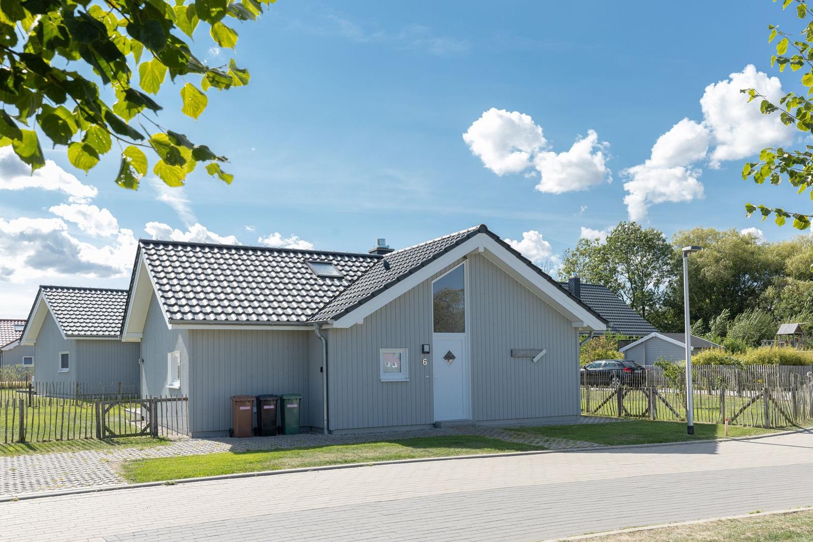 Moderne Ferienhaus mit grauer Fassade und schwarzem Dach unter blauem Himmel.