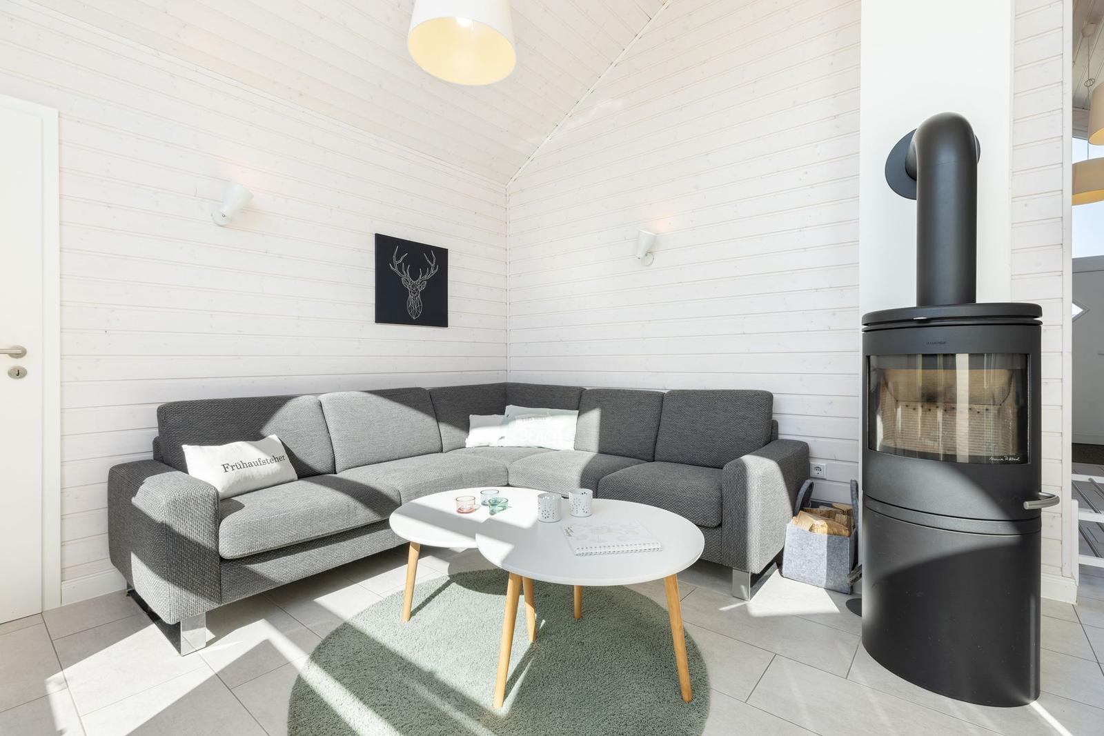 Wohnzimmer mit grauem Sofa, runder Tisch und Kaminofen.