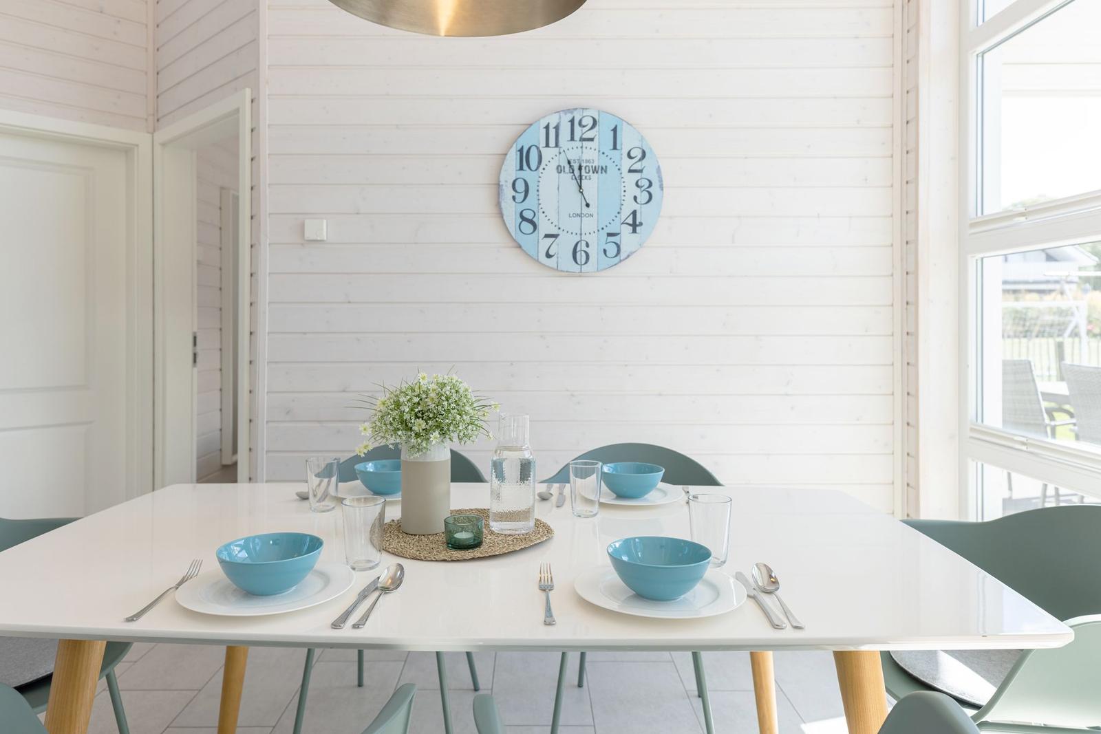 Esszimmer mit weißem Tisch, blauen Schalen und Wanduhr.