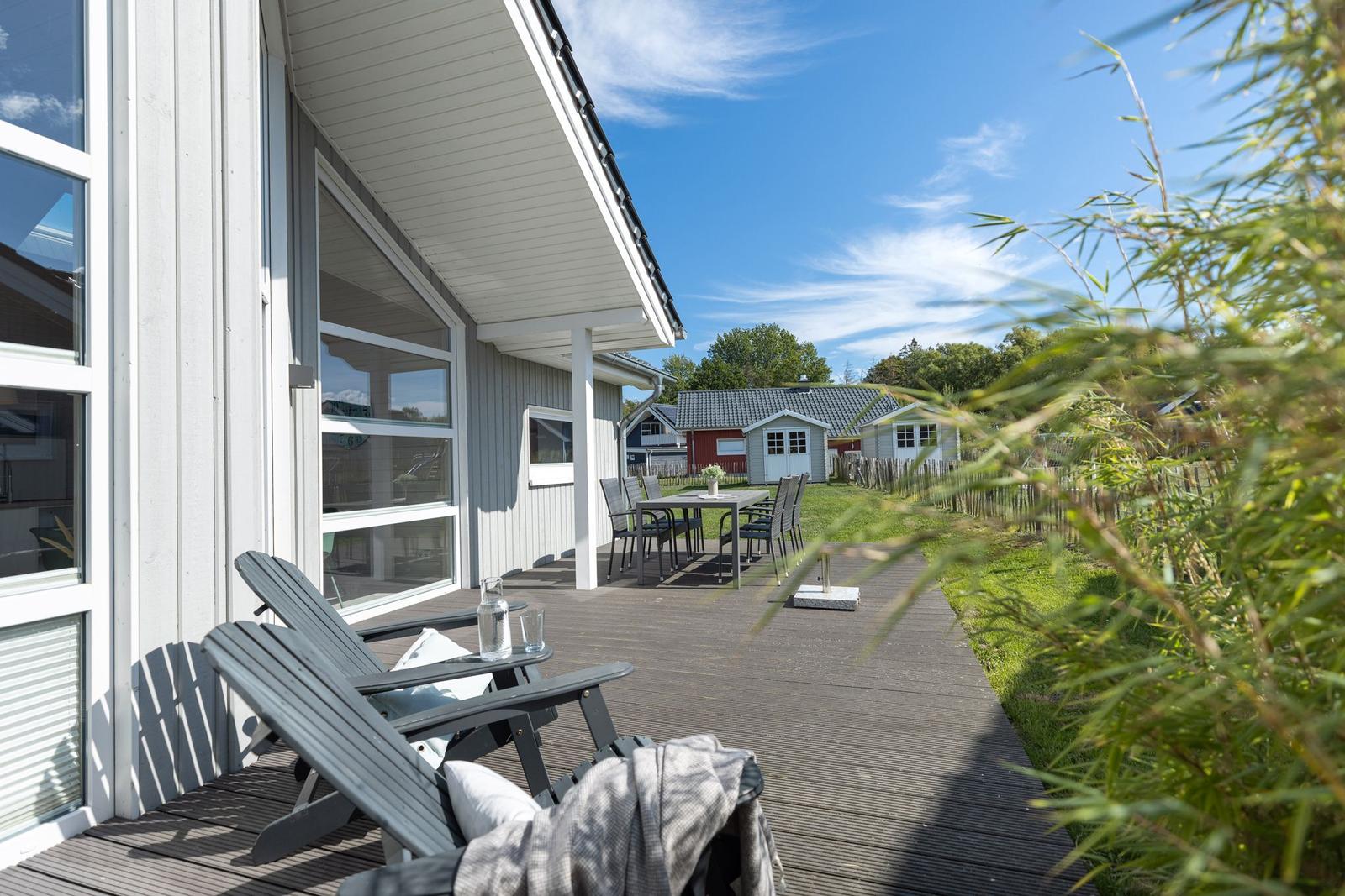 Terrasse mit Liegestühlen und Tisch, Blick auf Garten und Ferienhaus.