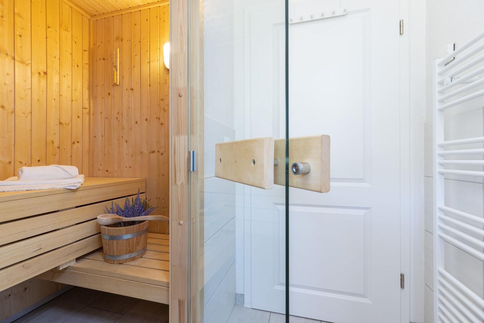 Sauna mit Holzbank und Lavendeltopf. Glaswand und Heizkörper daneben.