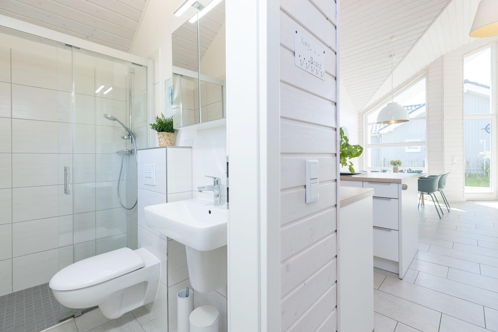 Badezimmer mit Dusche, Waschbecken und Toilette. Küche mit Küchentisch und Stühlen.