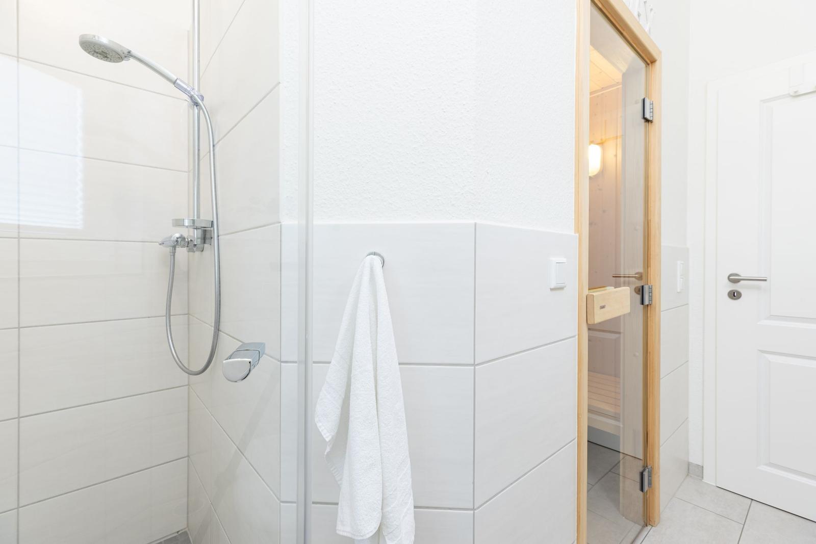 Dusche mit Duschbrause, Handtuch und Blick in Sauna.