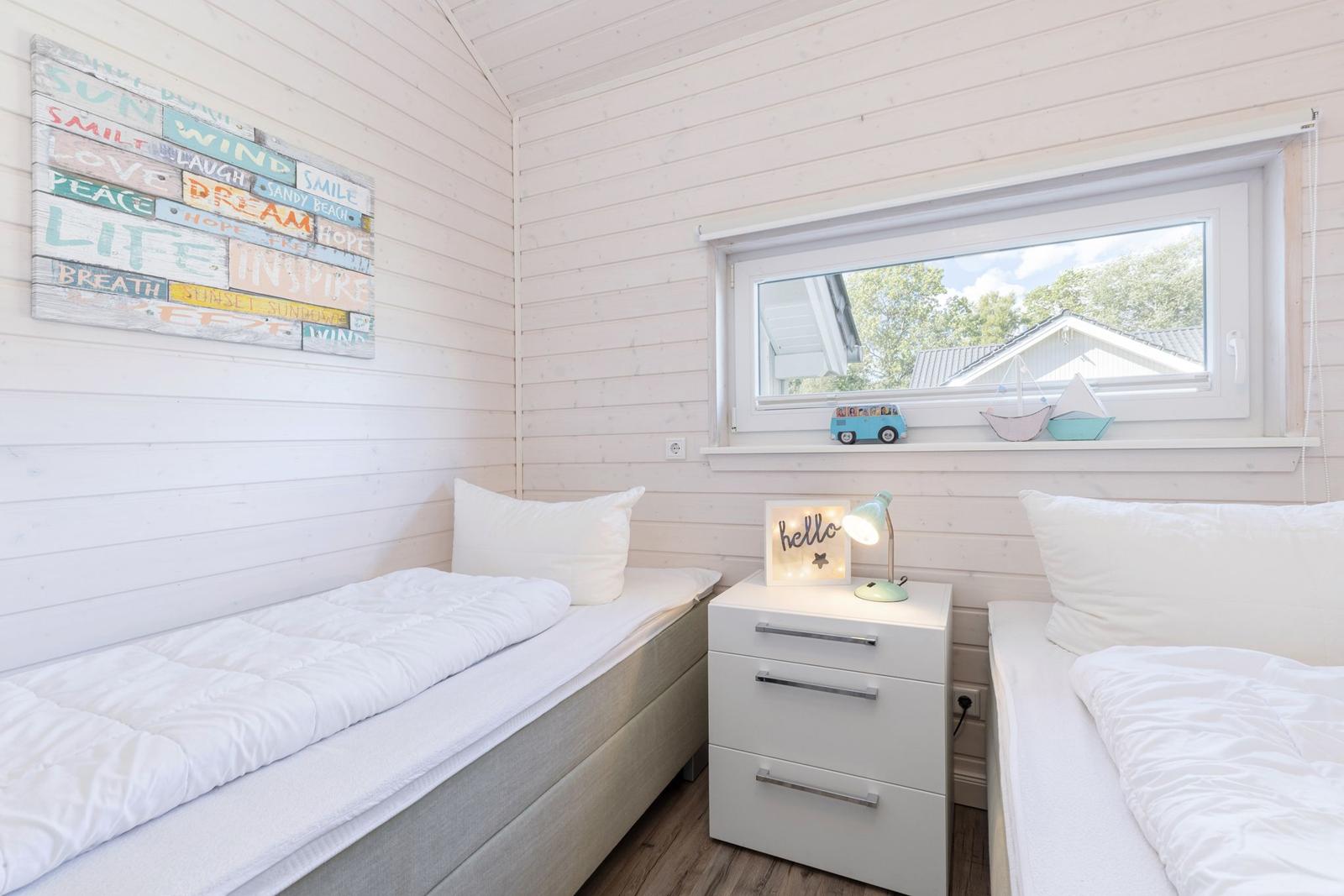 Zwei Betten mit weißen Laken, Nachttisch und Fenster mit Blick nach draußen.