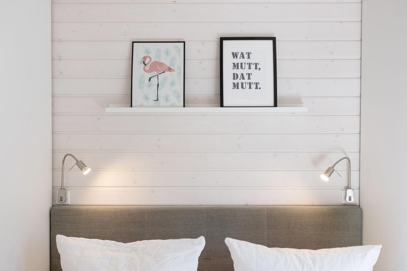 Schlafzimmer mit Kopfteil, Wandbildern und Nachttischlampen.