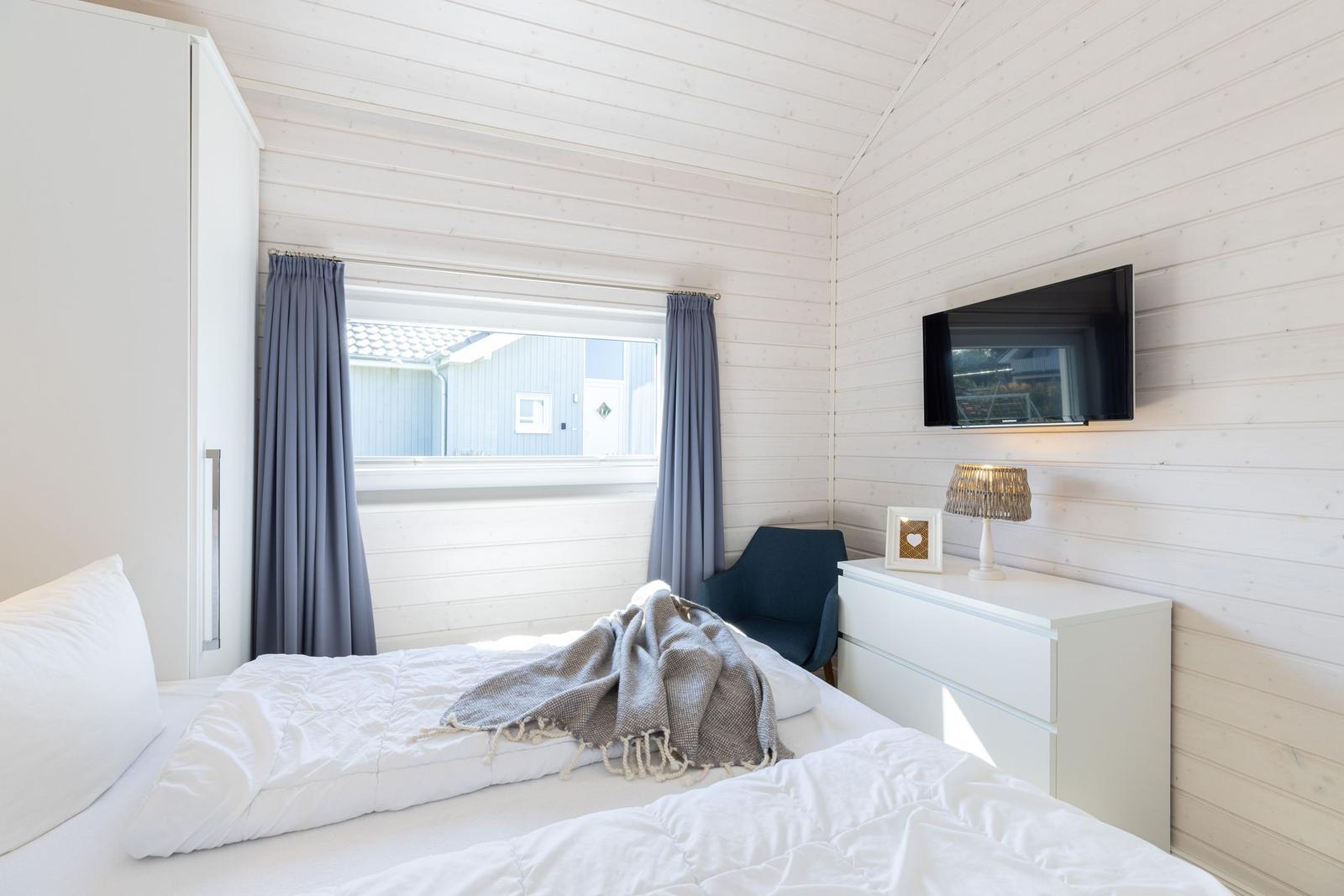 Schlafzimmer mit weißem Bett, Fenster und Wand-TV.