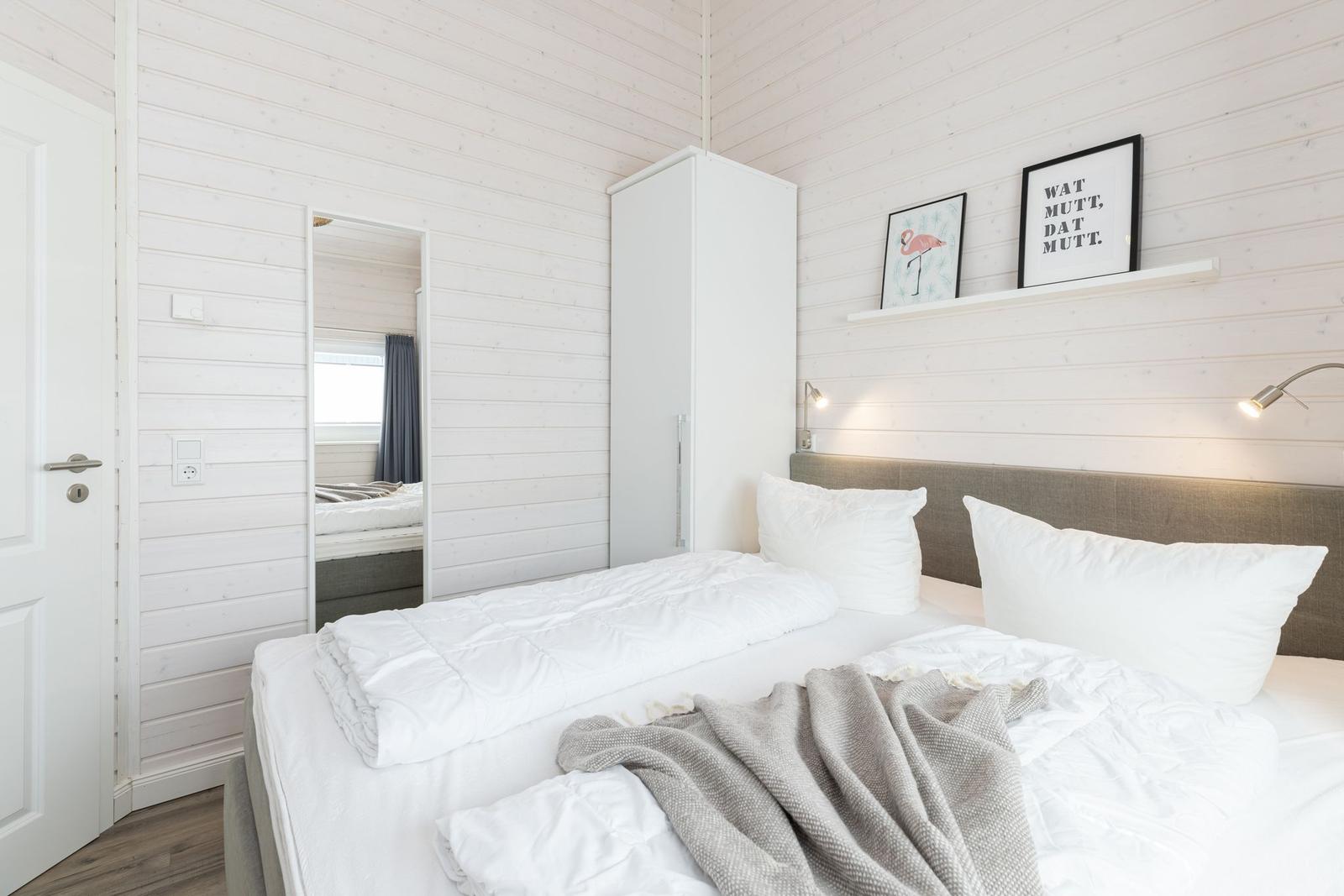 Schlafzimmer mit weißem Bett, Kleiderschrank und Wandbildern.