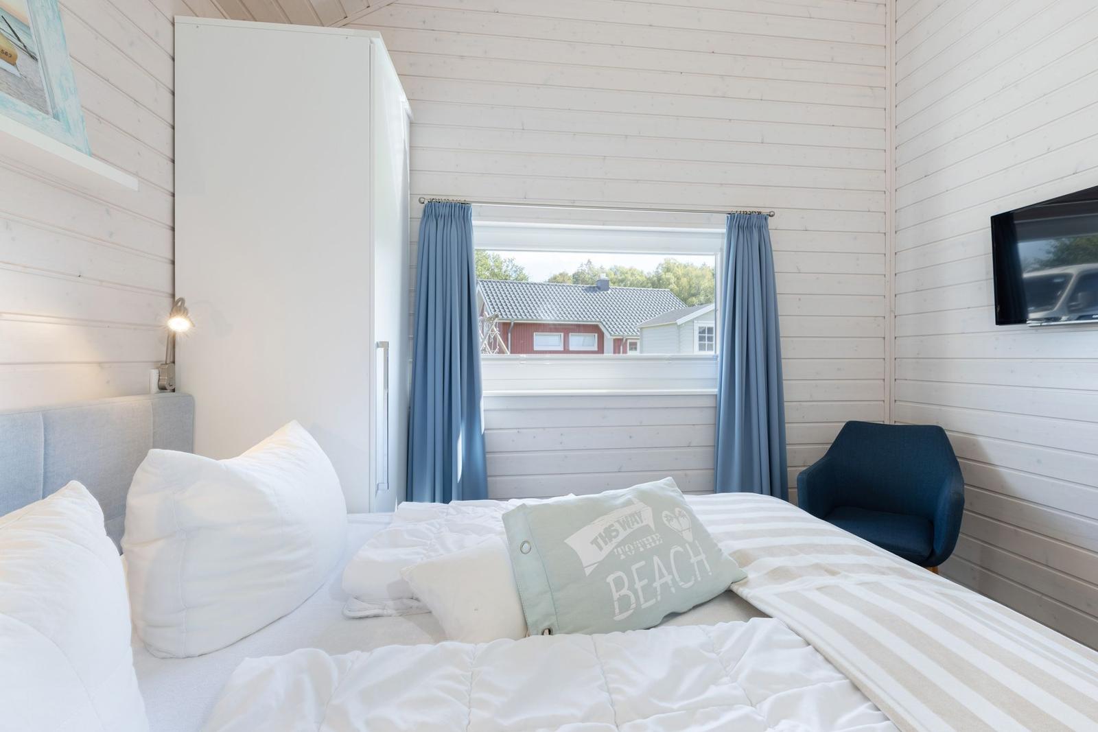 Schlafzimmer mit Bett, Fenster, Vorhängen und Sessel.