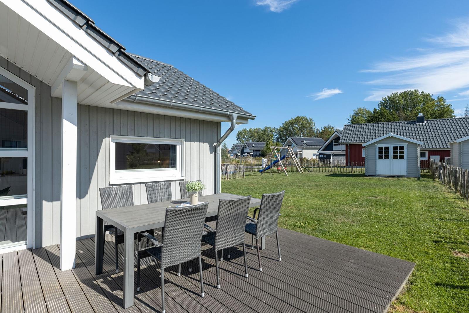 Terrasse mit Tisch und Stühlen. Grünfläche und Spielplatz im Hintergrund.