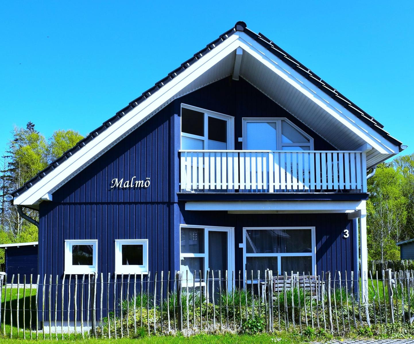 Blau gestrichenes Haus mit Balkon und Fenstern. Nummer 3. Umzäunt mit Holzzaun.