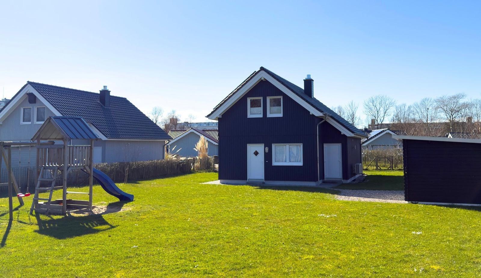 Schwarzes Holzhaus mit weißem Fensterrahmen und Spielplatz im Vorgarten.