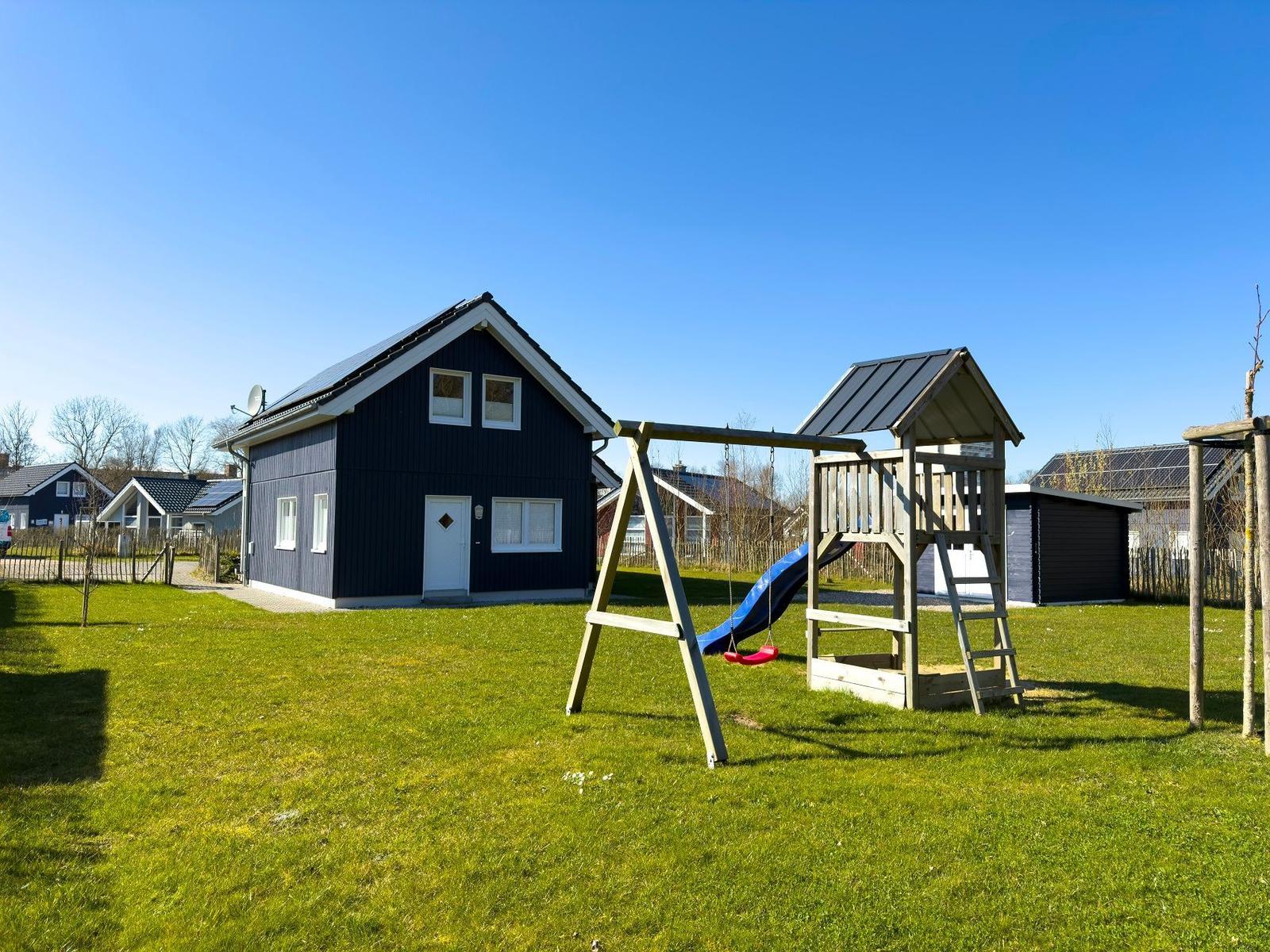 Ein Haus mit Spielplatz im Garten. Spielgeräte und grünes Gras sind sichtbar.