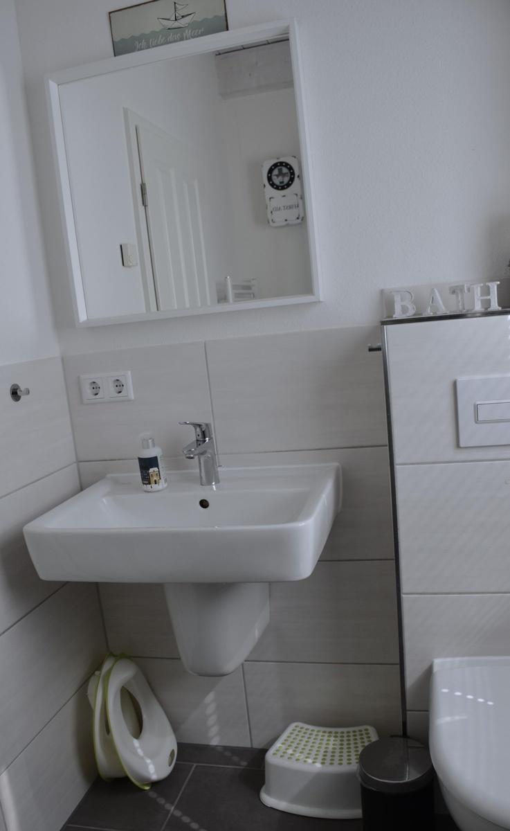 Badezimmer mit Waschbecken, Spiegel, Toilette und Stehleuchte.