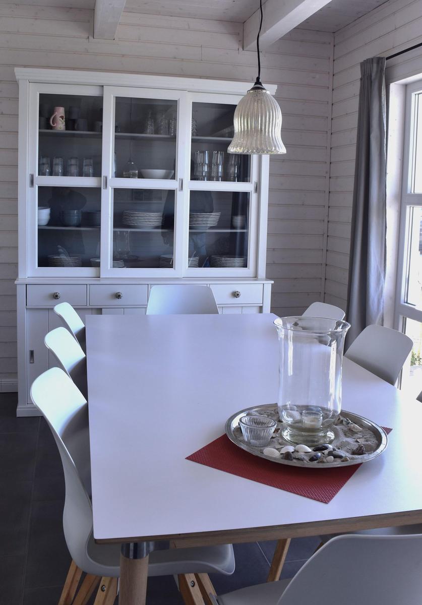 Esszimmer mit weißem Tisch, Stühlen und Schrank. Fenster und Deckenbalken sichtbar.