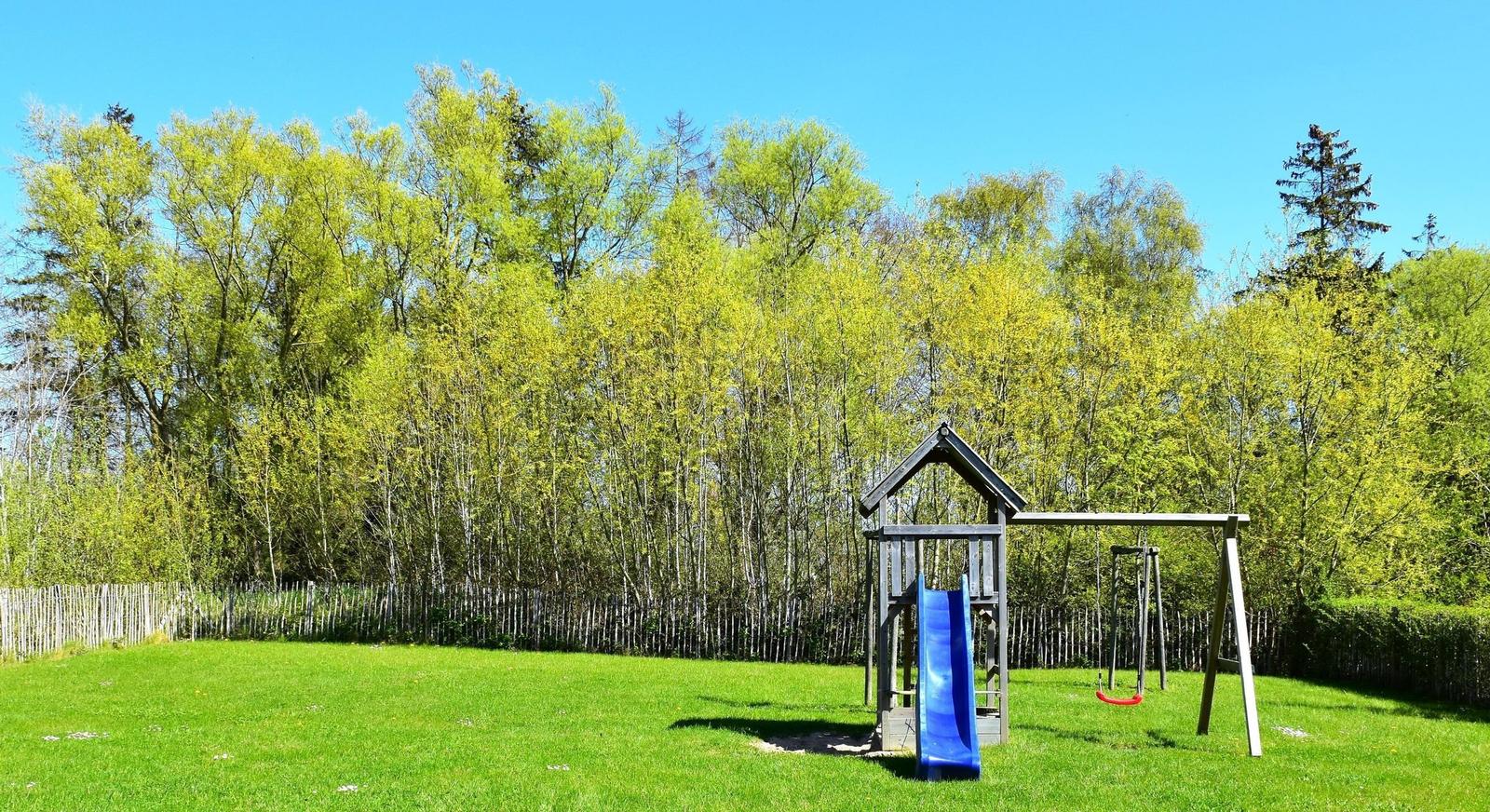Großer grüner Garten mit Spielplatz und Wald im Hintergrund.