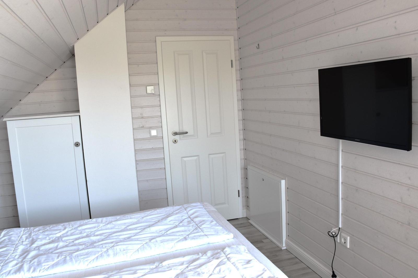 Schlafzimmer mit weißem Bett, Kleiderschrank und Wandfernseher.