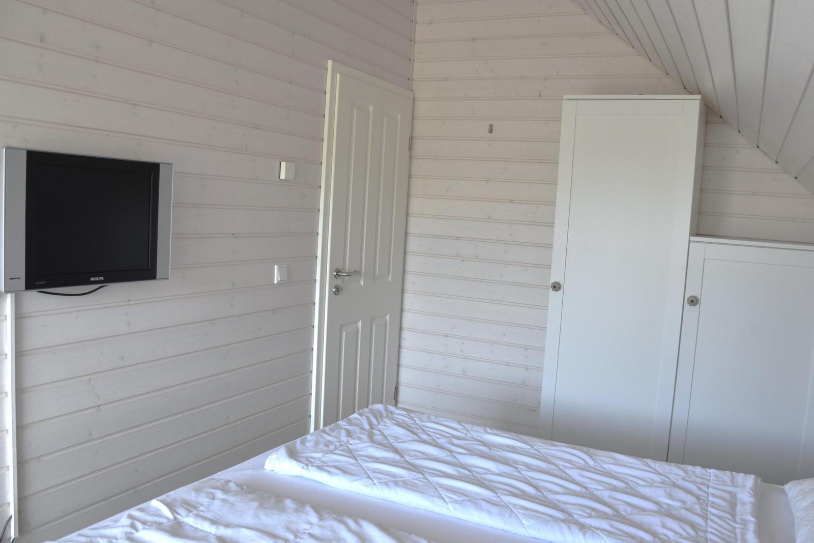 Schlafzimmer mit Bett, Schrank und Wandfernseher.
