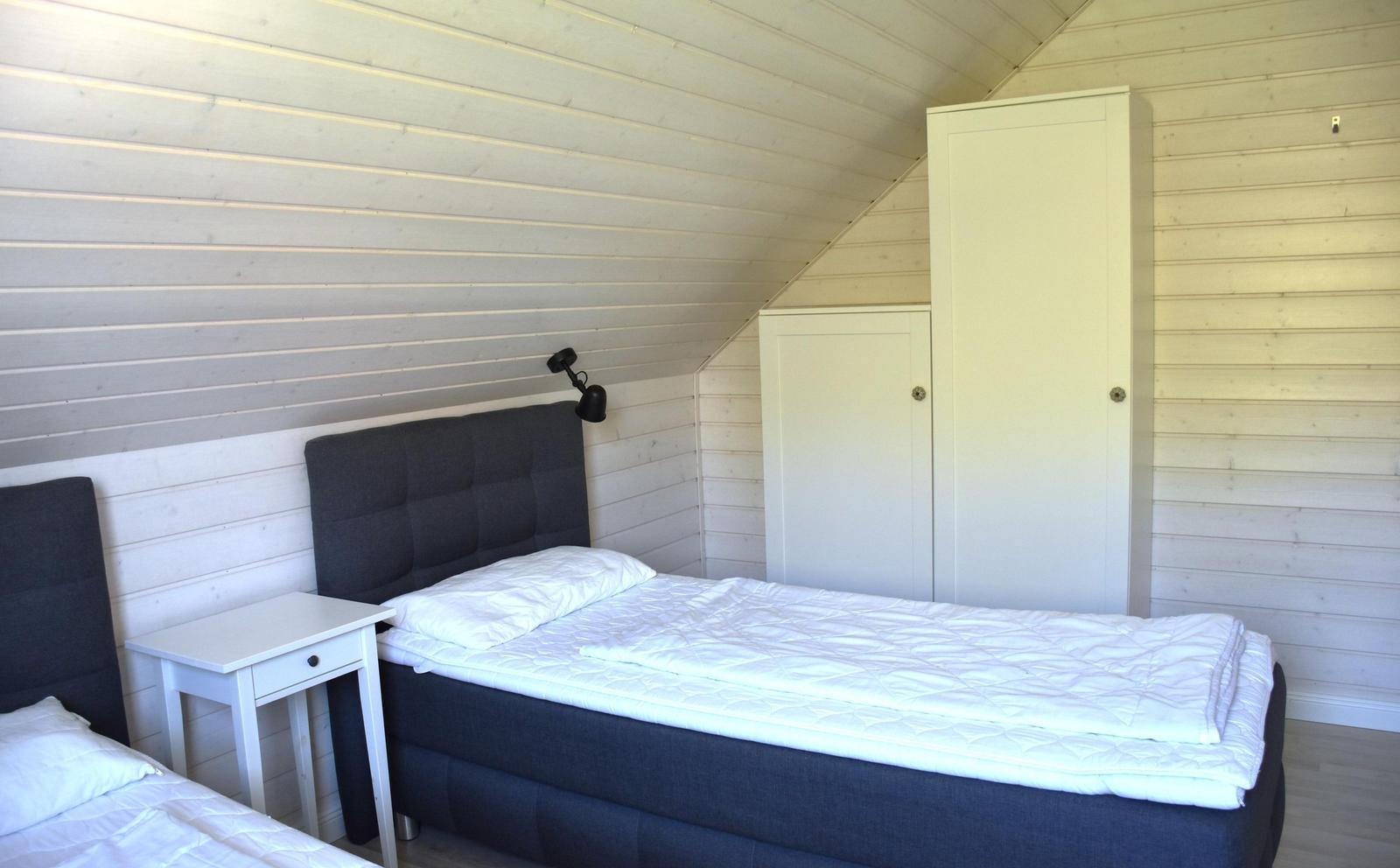 Zwei Betten mit weißen Bettwäschen, weiße Nachttische und Schränke in einem Raum mit Holzwandverkleidung.