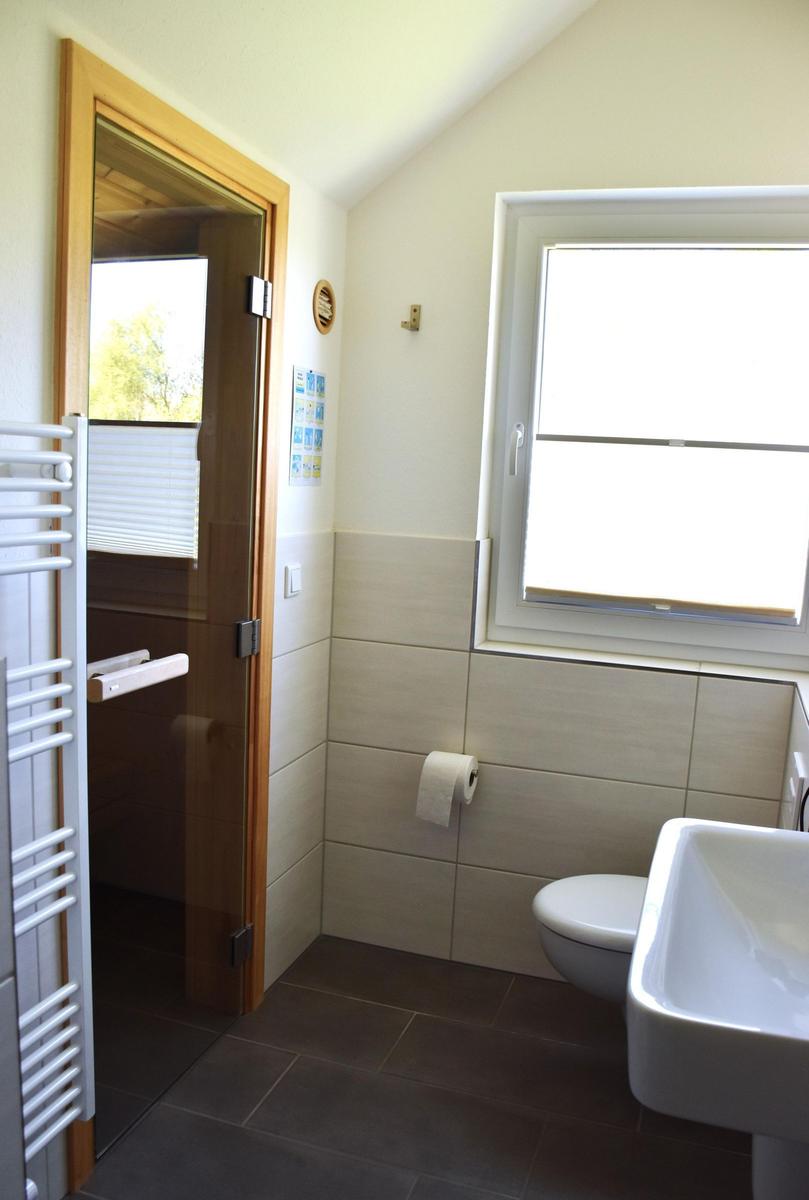 Badezimmer mit Toilette, Waschbecken und Dusche. Fenster sorgt für Tageslicht.