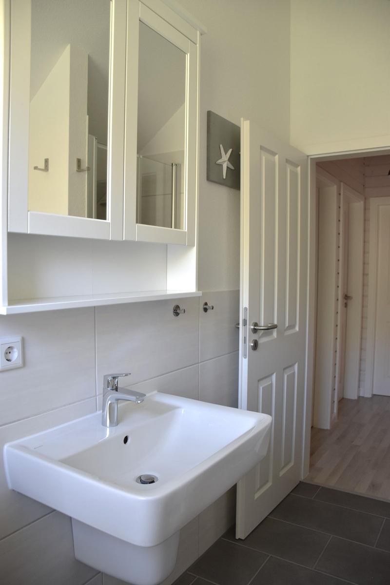 Badezimmer mit Waschbecken, Spiegelschrank und offener Tür zum Flur.