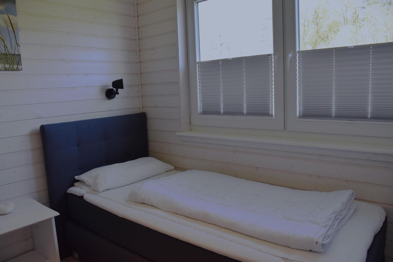 Ein Bett mit weißer Bettwäsche und dunklem Kopfteil neben einem Fenster mit Jalousien.