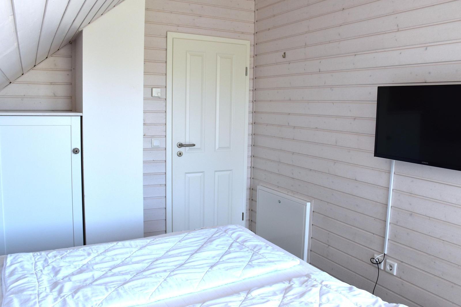 Schlafzimmer mit Bett, Kleiderschrank und Wandfernseher an Holzwand.