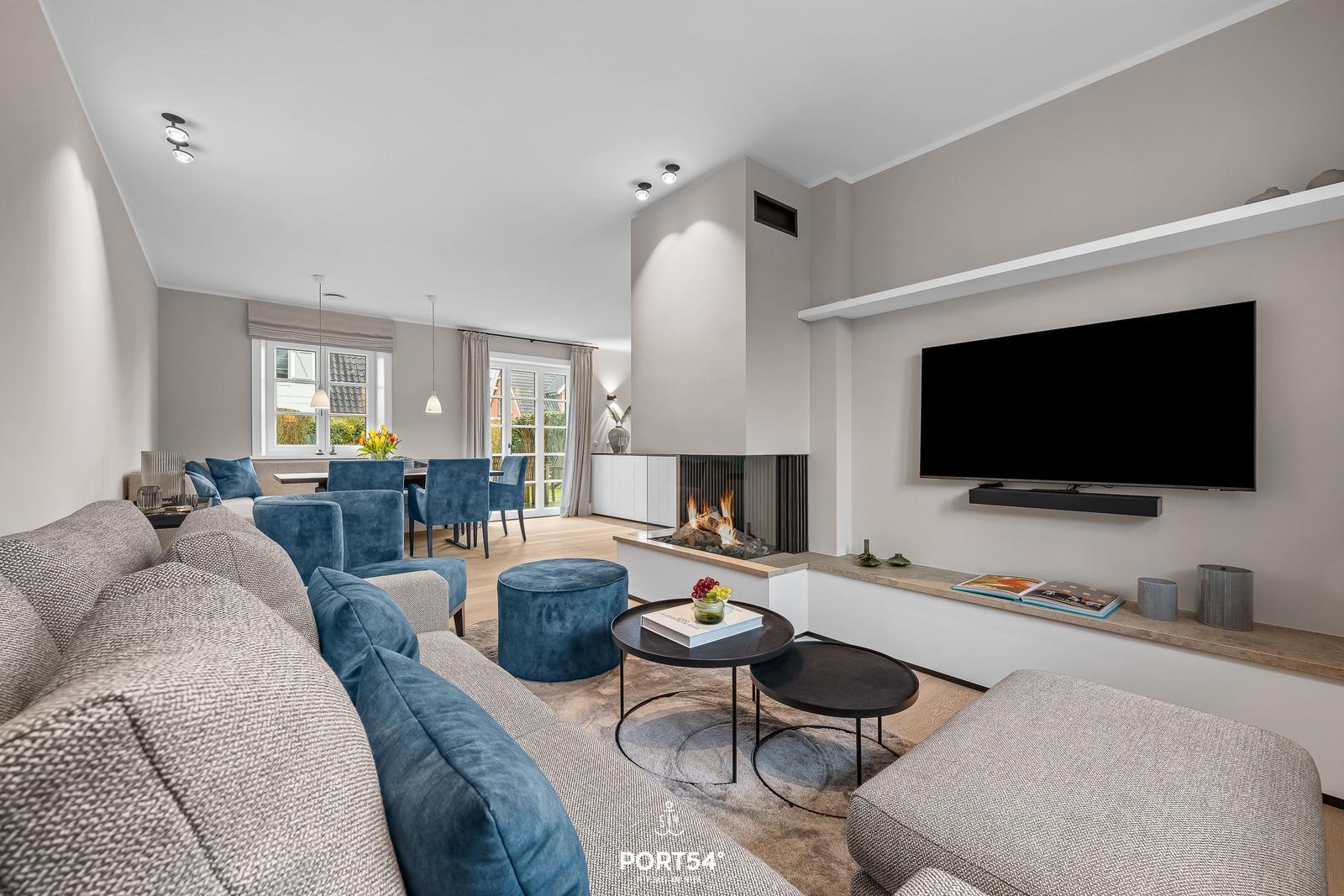 Wohn- und Essbereich mit Kamin, TV und blauen Sesseln.