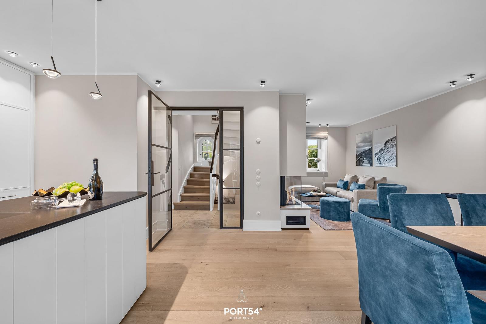 Offener Wohnbereich mit Essbereich, Küche und Treppenaufgang. Blaue Sessel und Kamin.