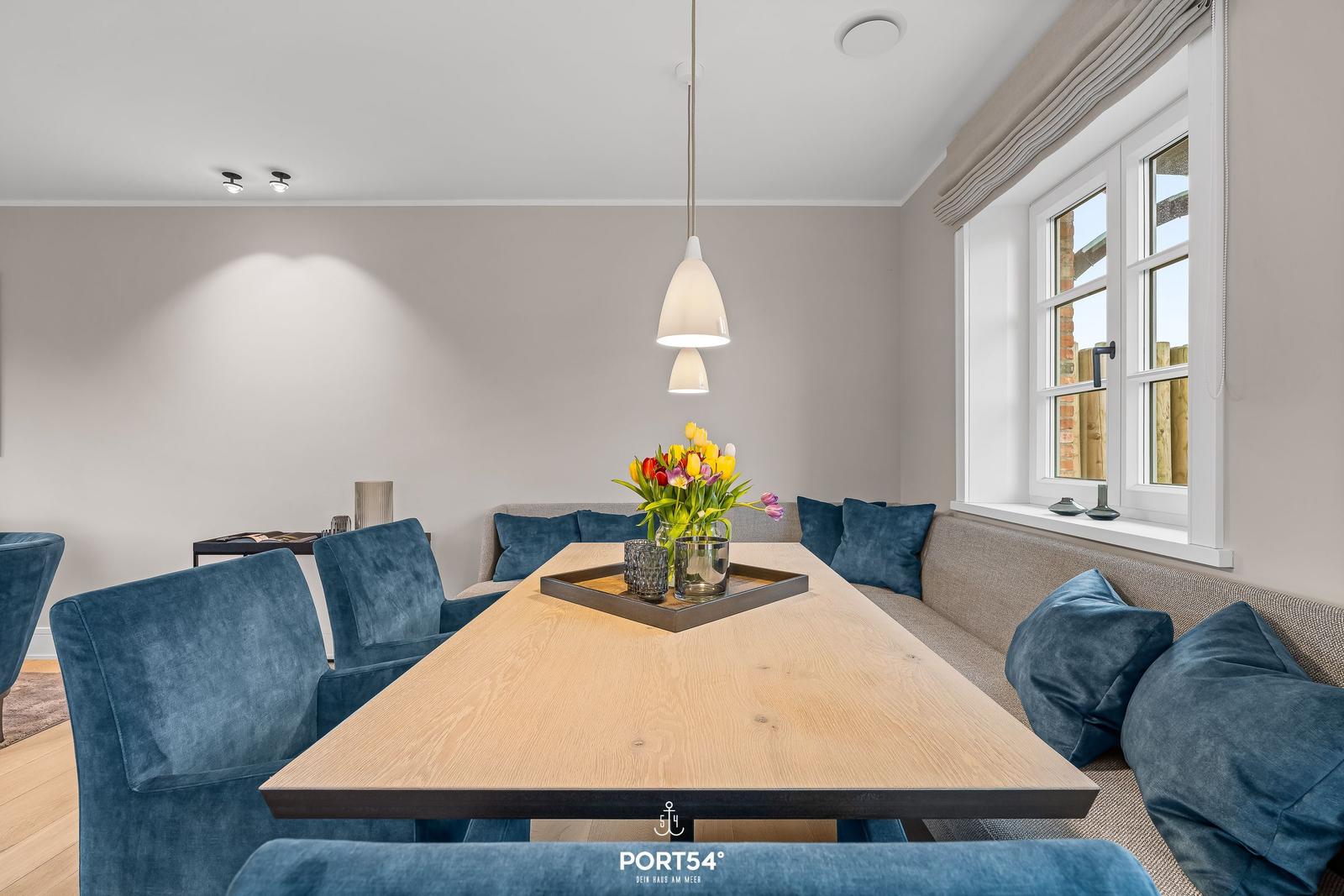 Esszimmer mit Holztisch, blauen Stühlen und Fensterblick.