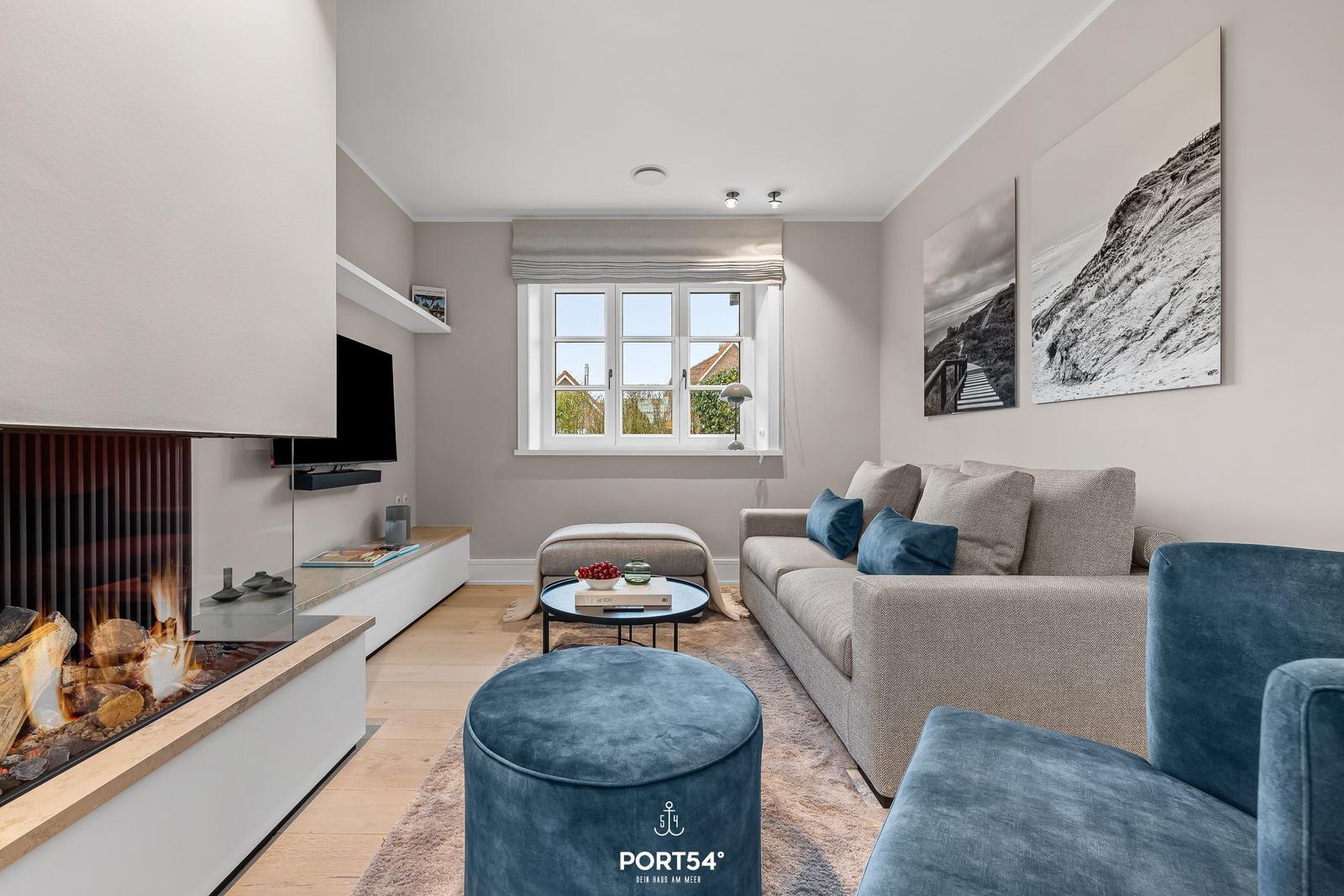 Wohnzimmer mit Kamin, Sofa und Fenster. Wandbilder und blauer Sitz.