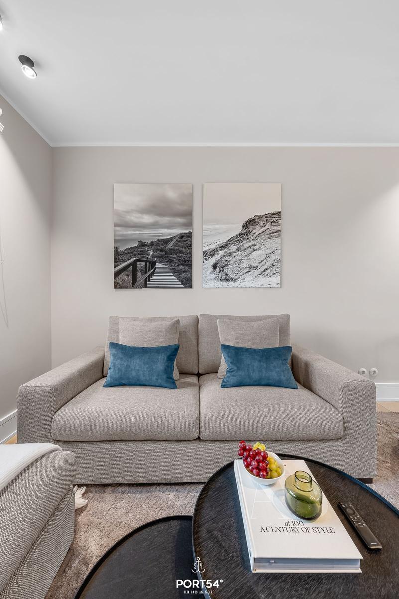 Ein Wohnzimmer mit grauem Sofa, zwei blauen Kissen und zwei Wandbildern über dem Sofa.