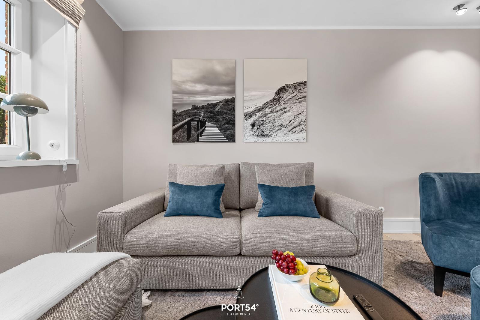 Wohnzimmer mit grauem Sofa, blauen Kissen und Wandbildern